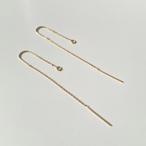 May include: A pair of gold chain earrings with a small circle charm on one earring. The earrings are long and dangle.