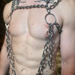 Op de afbeelding: Een zilveren ketting met meerdere strengen en een grote ringhanger. De ketting wordt om de nek en borst gedragen, met de ringhanger hangend in het midden van de borst.