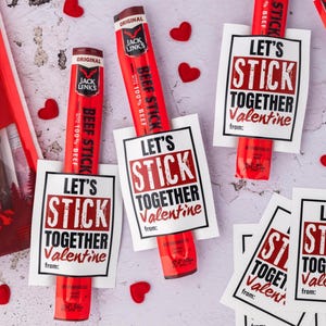 May include: Red beef sticks with Valentine's Day cards that read "Let's Stick Together Valentine." The cards are white with a black border and red text. Small red heart decorations are scattered around the sticks.