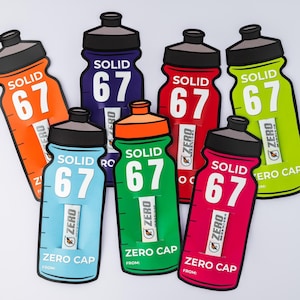May include: A selection of water bottle-shaped cutouts in various colours. Each cutout displays the word "SOLID" above the number "67". The cutouts are in shades of orange, blue, green, red, and pink, with black caps and the text "ZERO CAP".