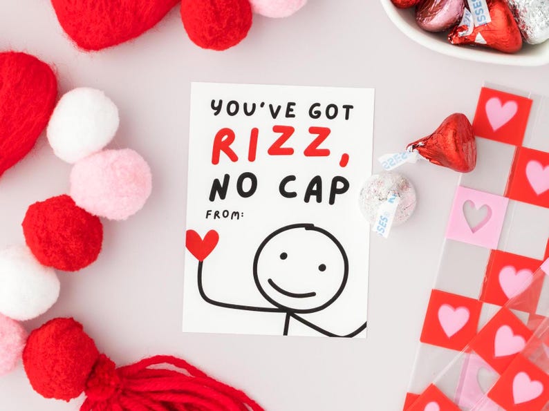 Op de afbeelding: Een witte kaart met zwarte en rode tekst die "You've got rizz, no cap" zegt met een stick figure tekening van een persoon met een hart boven zijn hoofd. De kaart is omringd door rode en roze pompoenen en rode en roze hartvormige stickers.