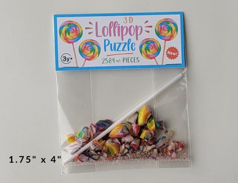 May include: A clear plastic bag containing a 3-D lollipop puzzle with 2584 pieces. The bag has a label that says "3-D Lollipop Puzzle" and "2584+ PIECES". The label also has a picture of a lollipop and the words "New!" and "3y+".