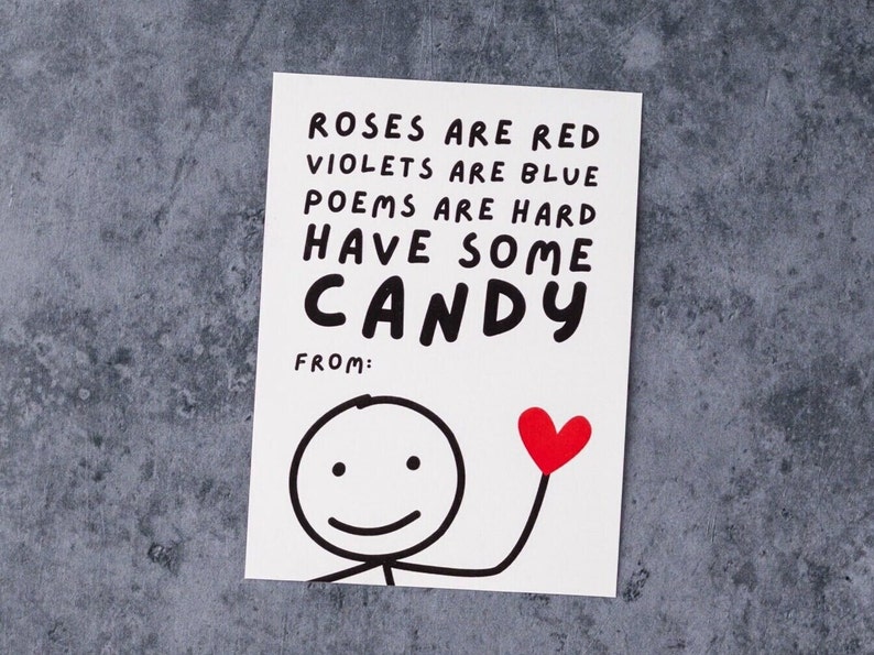 May include: A white greeting card with the text "Roses are red, violets are blue, poems are hard, have some candy" in black. A stick figure holds a red heart. The card is on a gray surface.