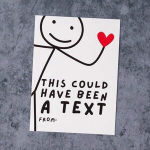 May include: A white card with a stick figure holding a red heart. The card reads "THIS COULD HAVE BEEN A TEXT" with a space for "FROM:" in black text. The background is a mottled gray surface.
