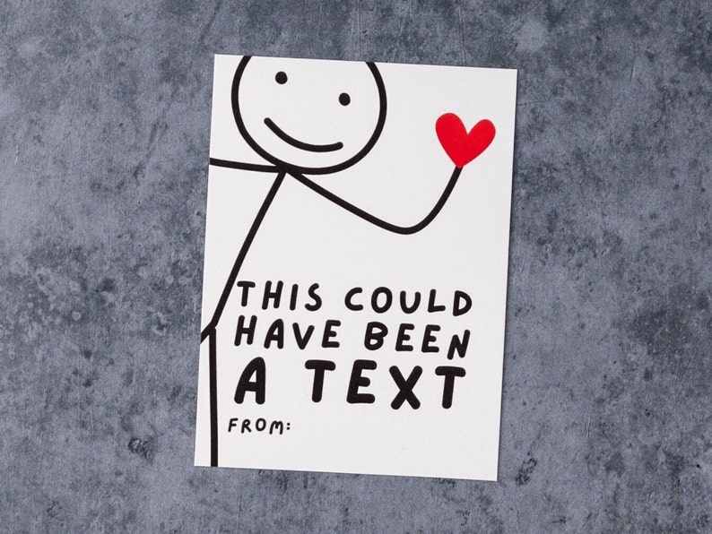 May include: A white card with a stick figure holding a red heart. The card reads "THIS COULD HAVE BEEN A TEXT" with a space for "FROM:" in black text. The background is a mottled gray surface.