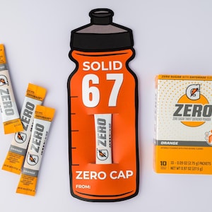 May include: An orange Gatorade Zero display featuring a bottle-shaped cutout with the text "SOLID 67" and "ZERO CAP". Includes packets and a box of orange-flavored Zero sugar thirst quencher powder. The box contains 10 packets, each 2.75 g.