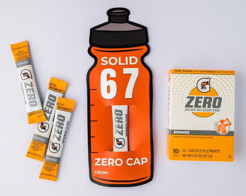 May include: An orange Gatorade Zero display featuring a bottle-shaped cutout with the text "SOLID 67" and "ZERO CAP". Includes packets and a box of orange-flavored Zero sugar thirst quencher powder. The box contains 10 packets, each 2.75 g.