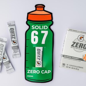 May include: A green and orange Gatorade Zero bottle-shaped display with the text "SOLID 67" and "ZERO CAP". Several Glacier Cherry flavour drink mix packets and a box of the same flavour are also present.