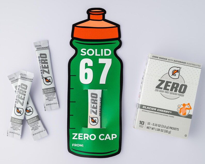 May include: A green and orange Gatorade Zero bottle-shaped display with the text "SOLID 67" and "ZERO CAP". Several Glacier Cherry flavour drink mix packets and a box of the same flavour are also present.