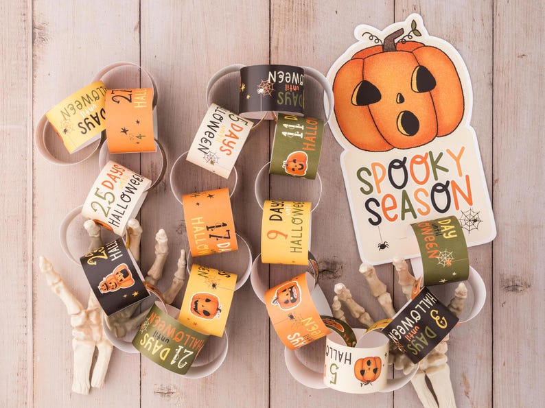 May include: A Halloween countdown chain with orange and black paper rings. Each ring has a number and the text "Days until Halloween". The chain is decorated with a spooky season sign featuring a pumpkin and spiderwebs.