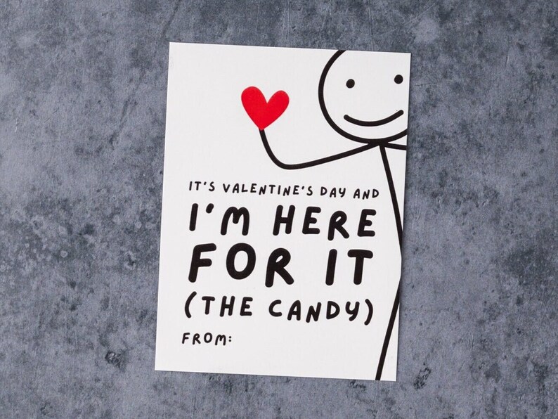 May include: A white Valentine's Day card with a stick figure holding a red heart. The card reads "IT'S VALENTINE'S DAY AND I'M HERE FOR IT (THE CANDY) FROM:" in bold black letters. The background is a textured gray surface.
