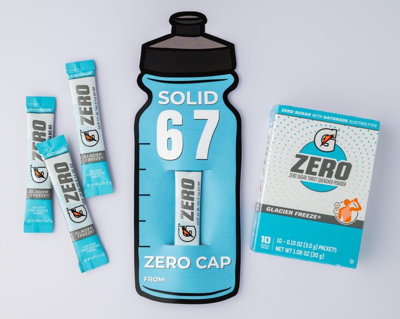May include: A promotional image featuring Gatorade Zero products. The image includes a large, blue bottle-shaped display with the text "SOLID 67" and "ZERO CAP." Several Glacier Freeze packets and a box of Zero sugar thirst quencher powder are also visible.
