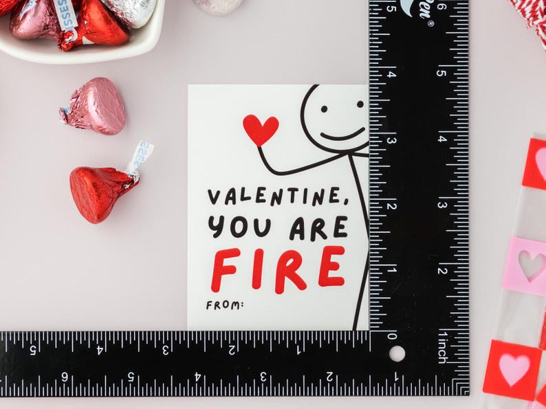 Op de afbeelding: Een witte kaart met een rood hart en een stick figure-illustratie. De kaart luidt "Valentine, you are fire" met het woord "fire" in rood. De kaart heeft ook de woorden "from:" onderaan.