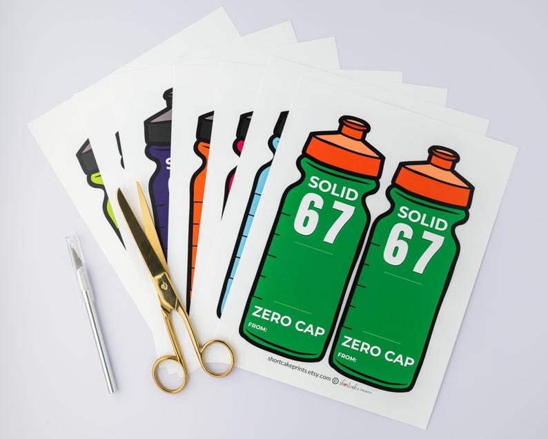 May include: A selection of water bottle stickers in different colours, including green, orange, purple, and blue. The stickers display the text "SOLID 67" and "ZERO CAP". Gold scissors and a silver craft knife are also visible.