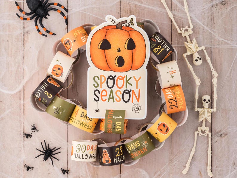 May include: A Halloween countdown chain with orange and black paper rings featuring numbers and the text "Days until Halloween". A large orange pumpkin with a spooky face and the text "Spooky Season" is in the center. Two white skeletons are on either side of the chain.