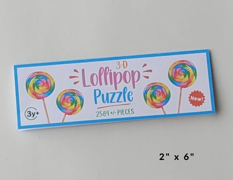 May include: A 3-D lollipop puzzle with 2584 pieces. The box features a colorful lollipop design and the text "3-D Lollipop Puzzle" and "2584+-PIECES". The box also has a "New!" sticker and a 3+ age recommendation.