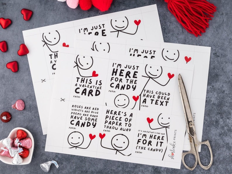 May include: Sheets of Valentine's Day cards with stick figure illustrations and humorous text. The cards feature phrases like "I'm just here for the candy" and "This is a Valentine card." Scissors and candy hearts are also visible.