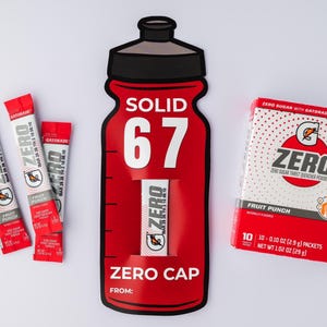 May include: A red and white Gatorade Zero Fruit Punch product display. The display includes a large bottle-shaped cutout with the word "SOLID" and the number "67". There are also three individual packets and a box of the drink mix.
