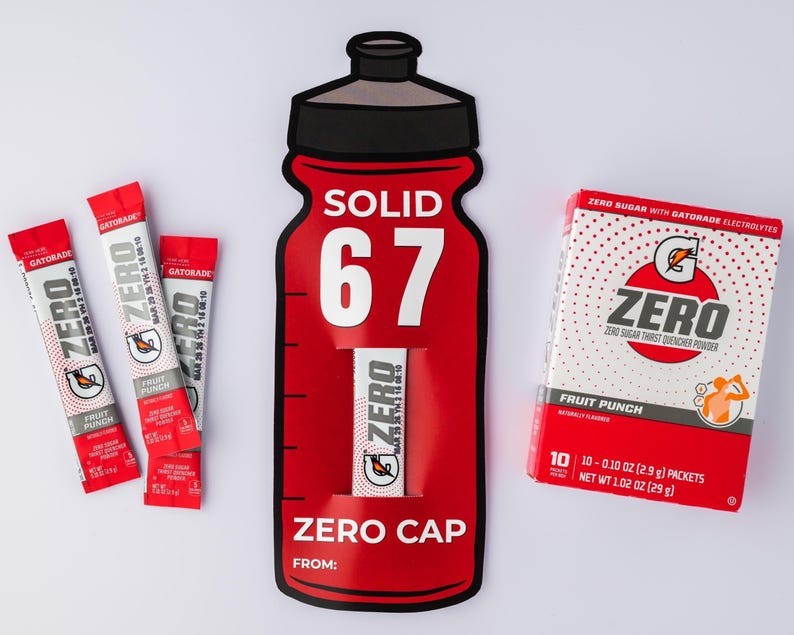 May include: A red and white Gatorade Zero Fruit Punch product display. The display includes a large bottle-shaped cutout with the word "SOLID" and the number "67". There are also three individual packets and a box of the drink mix.