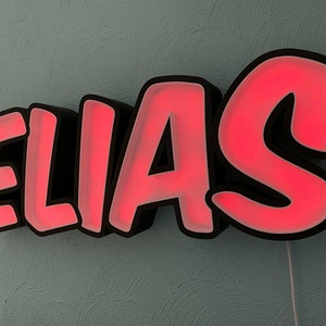 May include: A black and red neon sign with the name "ELIAS" in a bold, cartoon-style font.