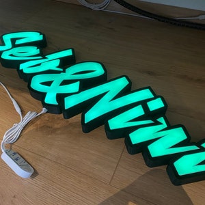 May include: A green illuminated sign with the word "Seveninn" in a stylized font. The sign is made of black plastic and has a white cord.