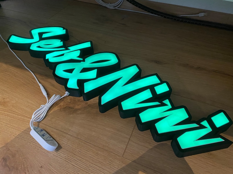 May include: A green illuminated sign with the word "Seveninn" in a stylized font. The sign is made of black plastic and has a white cord.