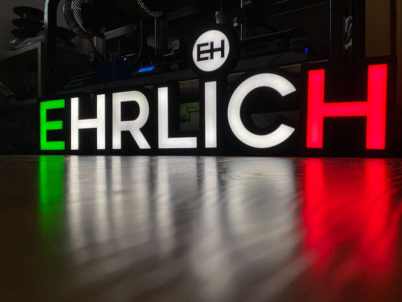 May include: A black sign with the word "EHRLICH" in white letters. The first letter "E" is green, and the last letter "H" is red.