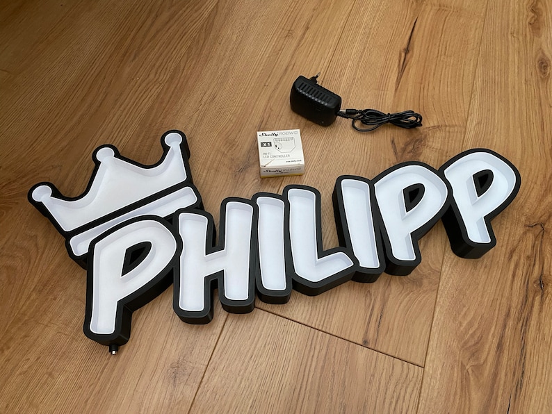 May include: Black and white light-up sign with the name "PHILIPP" in a cartoon font. The sign has a white crown on the left side.