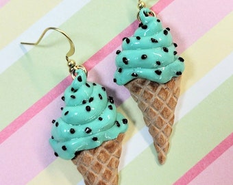 May include: A pair of mint green ice cream cone earrings with black chocolate chips. The earrings are made of polymer clay and have gold hooks.