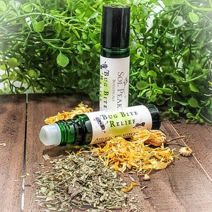 May include: Two green glass roller bottles with white labels that say "Sol Peak Botanicals Bug Bite Relief". The bottles are on a wooden surface with dried herbs and flowers.