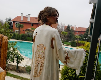 Może przedstawiać: Kremowy szlafrok w stylu kimono z wzorem lamparta. Szlafrok ma dużą twarz lamparta na plecach i mniejsze figury lamparta. Szlafrok ma szerokie rękawy i obszycie z frędzlami. Tło obejmuje basen i domy.