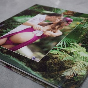 Op de afbeelding: Een fotoalbum met een groene en bruine omslag met een stel dat babyschoentjes vasthoudt in een tropische omgeving.