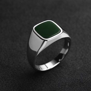 May include: A silver signet ring with a square, dark green stone. The ring has a polished, reflective surface and a classic, minimalist design. The dark green stone is set in a silver bezel.