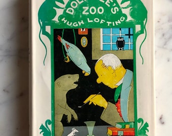Puede incluir: Una cubierta de libro vintage con un borde verde que presenta a un doctor con barba blanca, un loro, un oso y un ratón. El título del libro es "El Zoo del Doctor Dolittle" de Hugh Lofting.