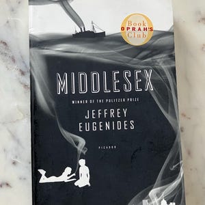 May include: A black and white book cover with the title "Middlesex" in large white letters. The book is by Jeffrey Eugenides and is a winner of the Pulitzer Prize. The cover also features a ship in the distance and a silhouette of two people.