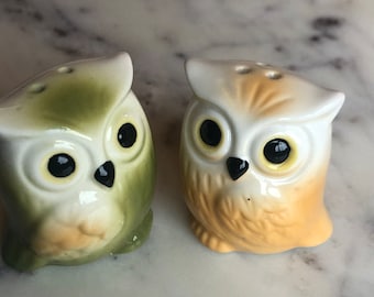 May include: Two ceramic owl salt and pepper shakers. The owl on the left is green and white, while the owl on the right is orange and white.