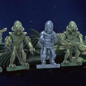 May include: Five miniature figures, four are green and one is silver. The green figures are humanoid with large heads and large eyes. The silver figure is wearing armor and a helmet. The figures are posed in a fighting stance.