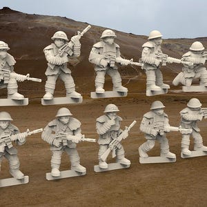 May include: A collection of ten off-white miniature soldier figurines, each holding a rifle. The figures are in various poses, some kneeling, others standing, and are mounted on rectangular bases. The background is a blurred landscape.