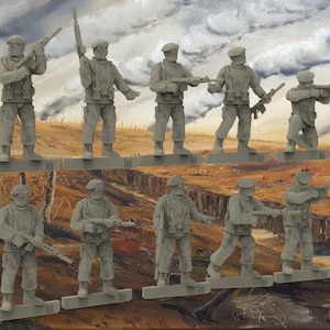 May include: Ten grey plastic toy soldiers in various poses, holding rifles, standing on a brown and green painted surface. The soldiers are wearing berets and have a military appearance.