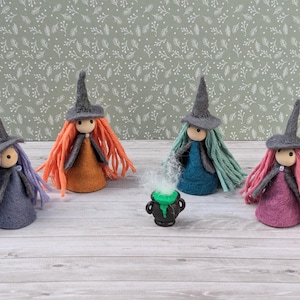May include: Five felt witch dolls with different coloured hair and dresses, standing around a small black cauldron with green liquid and steam coming out of it.