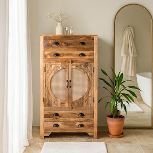 Könnte beinhalten: Ein hellbrauner Holzschrank mit Schubladen und Türen. Der Schrank hat ein gewebtes kreisförmiges Design an den Türen und schwarze Beschläge. Der Schrank befindet sich in einem Badezimmer mit einem Spiegel und einer Topfpflanze.