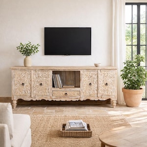 Könnte beinhalten: Ein helles TV-Möbel aus Holz mit geschnitzten floralen Mustern. Es verfügt über mehrere Schränke, Schubladen und ein offenes Regal für Medienkomponenten. Ein schwarzer Flachbildfernseher ist darüber montiert. Ein gewebter Teppich und eine Topfpflanze befinden sich im Vordergrund.
