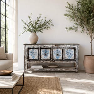 Op de afbeelding: Een rechthoekig houten dressoir met vier kastdeuren voorzien van handgeschilderde blauwe en witte bloemenurnmotieven. Het frame heeft een verweerde zwart-witte afwerking met uitgesneden bladpatronen en bevat een open onderste plank voor opslag.