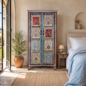 Könnte beinhalten: Ein hoher, rechteckiger Holzschrank mit zwei Türen und acht einzelnen Paneelen. Jedes Paneel zeigt komplizierte, farbenfrohe Blumen- und Paisley-Muster in Rot-, Blau- und Weißtönen. Der Rahmen ist mit dekorativen Bordüren bemalt.