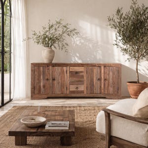 Puede incluir: Un aparador rústico de madera con múltiples puertas y cajones. El mueble está hecho de madera recuperada, mostrando un acabado natural y envejecido. Una mesa de centro y una silla están frente al aparador. Un jarrón con ramas está encima.