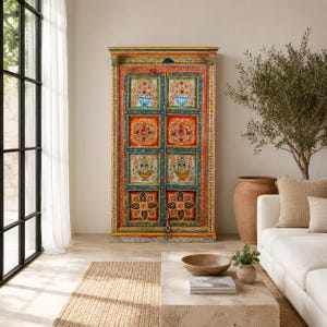 Op de afbeelding: Een hoge, rechthoekige houten kast met twee deuren voorzien van handgeschilderde bloemmotieven in levendige tinten oranje, blauw, geel en groen. De kast heeft een decoratief frame met ingewikkelde patronen en een metalen grendel onderaan.