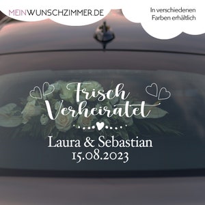 Könnte beinhalten: Weißer Autoaufkleber für die Heckscheibe mit dem Text "Frisch Verheiratet" mit zwei Herzen auf jeder Seite. Unter dem Text steht "Laura & Sebastian" und das Datum "15.08.2023".
