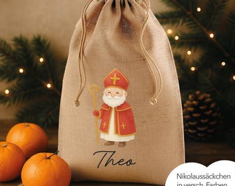 May include: A burlap drawstring gift bag featuring a cartoon illustration of Santa Claus in red and white attire, holding a gold staff. The name "Theo" is printed below the illustration. Oranges are in the foreground.