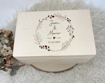 Puede incluir: Una caja de madera con un diseño de corona de flores grabado en la tapa. La corona incluye los nombres "Jessi & Mario" y la fecha "14. Juli 2023".