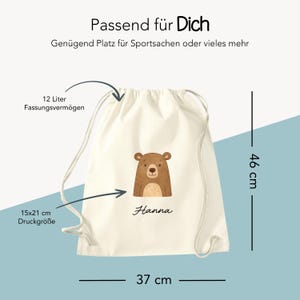 Puede incluir: Una bolsa con cord&oacute;n de color crema con un gr&aacute;fico de oso marr&oacute;n y el nombre "Hanna". La bolsa mide 37 cm de ancho y 46 cm de alto, con una capacidad de 12 litros. El &aacute;rea de impresi&oacute;n es de 15x21 cm. El texto "Passend f&uuml;r Dich" est&aacute; en la parte superior.